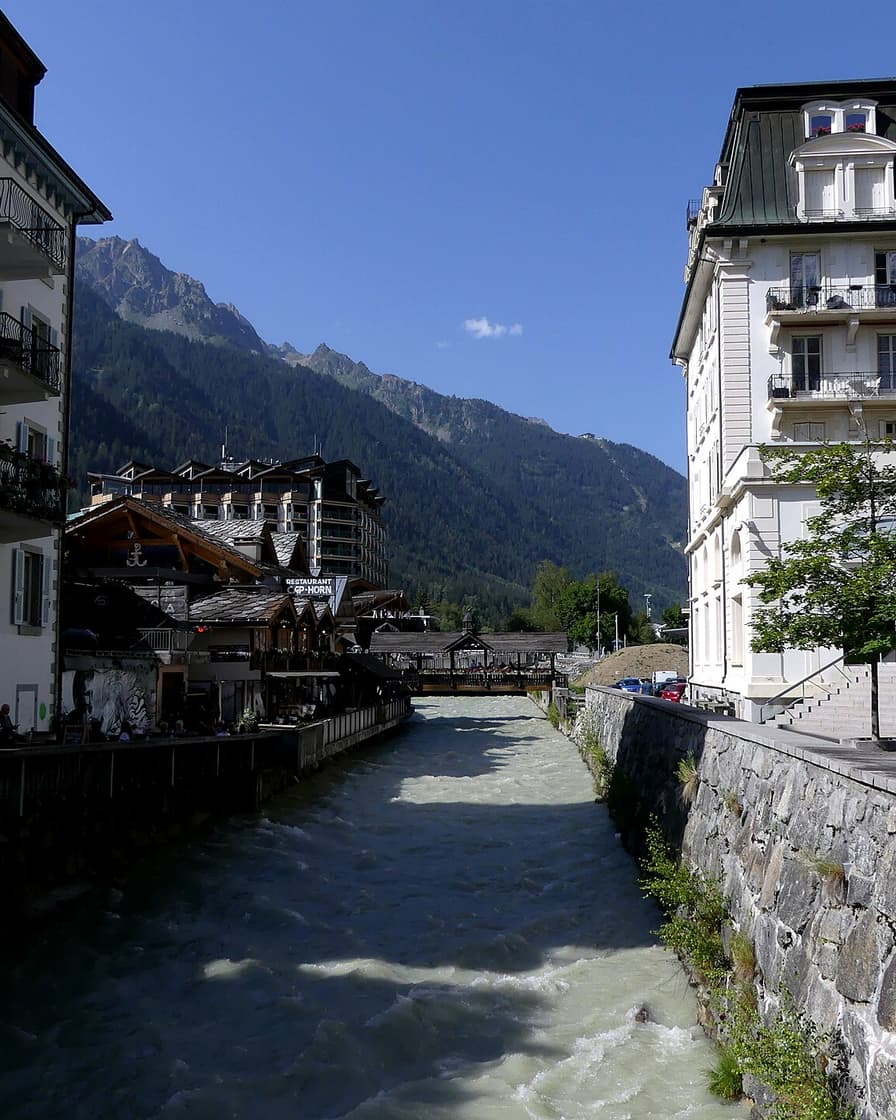 L'Arve traverse le centre de Chamonix entre des façades Belle Époque et des chalets de restaurants, au pied des aiguilles boisées du Brévent