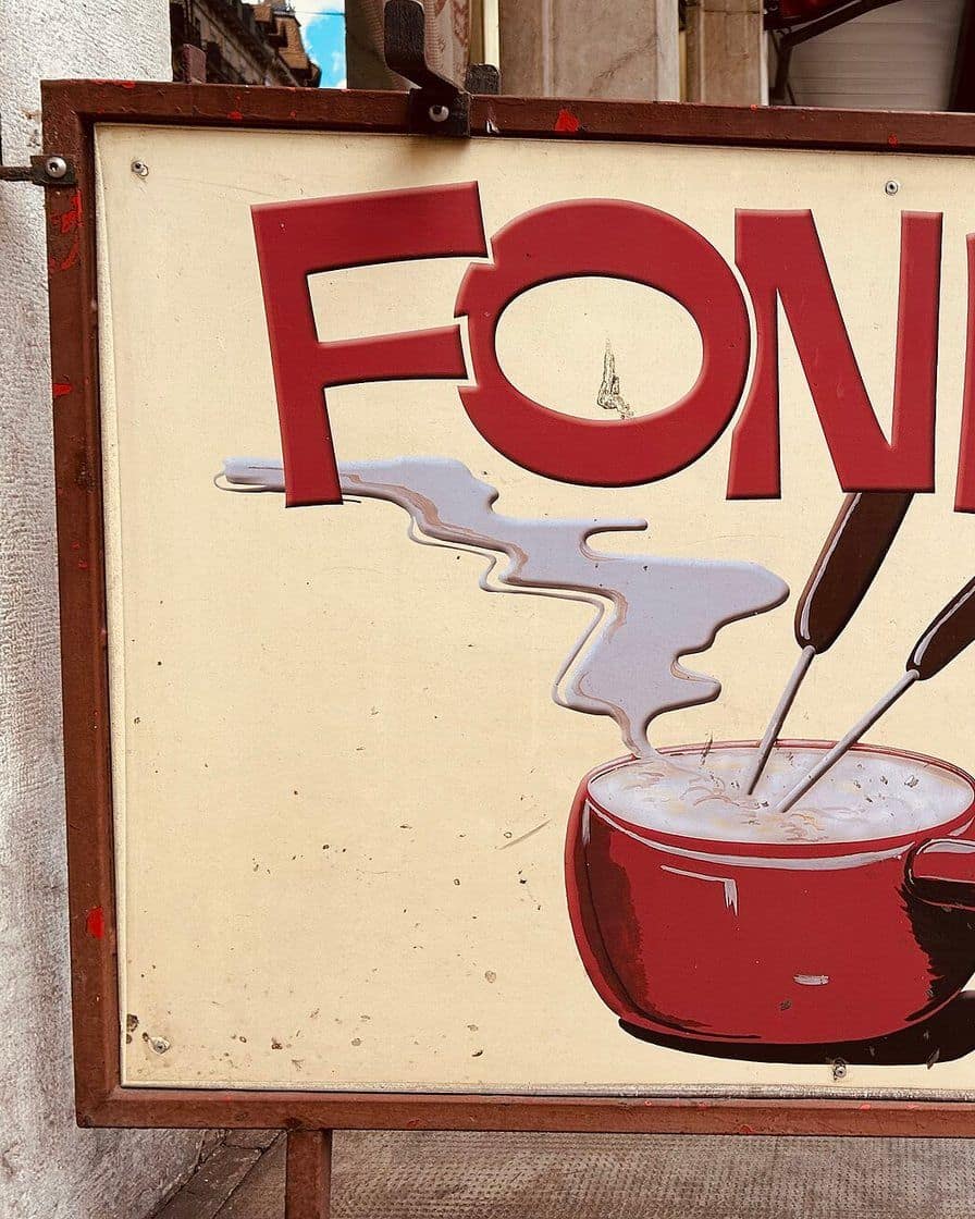 Caquelon de fondue au fromage fumant sur un réchaud, avec des cubes de pain piqués sur de longues fourchettes, sur une table en bois