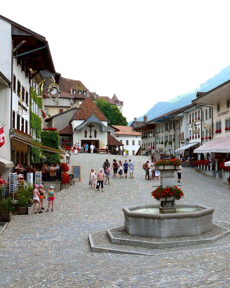 La rue principale pavée du village médiéval de Gruyères et son château sur la colline, dans les Préalpes fribourgeoises