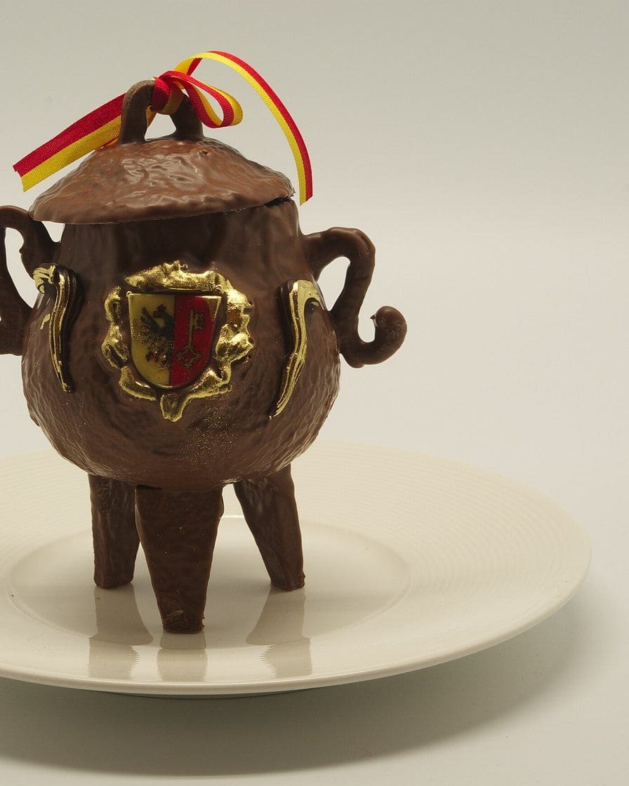 Marmite de l'Escalade en chocolat aux couleurs de Genève, entourée de légumes en massepain, dans une vitrine de chocolatier genevois